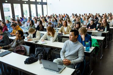 Ein großer heller Hörsaal mit vielen Studierenden an ihren Plätzen.