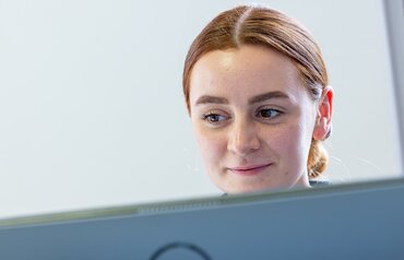 Eine Studentin blickt lächelnd auf einen Bildschirm.