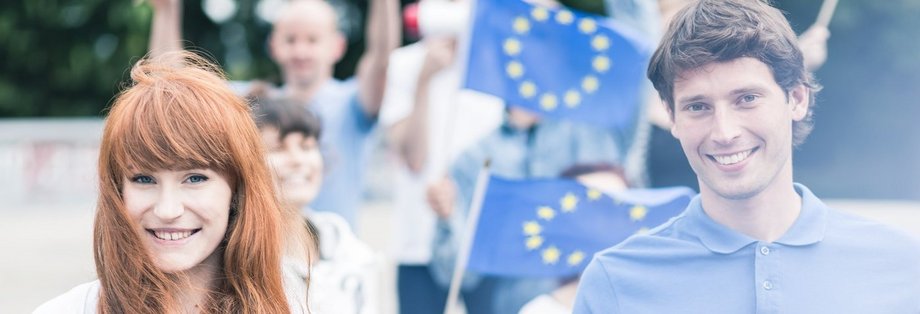 Eine Gruppe von jungen Menschen hält Europaflaggen hoch.