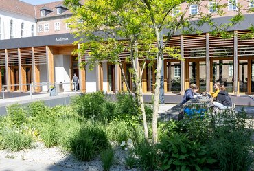 Vier Studierende sitzen im Außengelände an einen Tisch und lernen.


