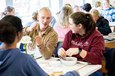 Mehrere Studierende sitzen in der Cafeteria an einem Tisch zusammen und essen.