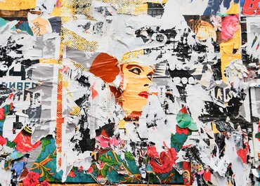 collagenartige, bunte Plakatwand mit teils abgerissenen Motiven. In der Mitte ist die Grafik eines  weiblichen Gesichtes zu sehen.