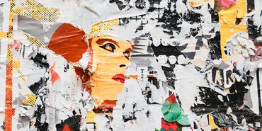 collagenartige, bunte Plakatwand mit teils abgerissenen Motiven. In der Mitte ist die Grafik eines  weiblichen Gesichtes zu sehen.