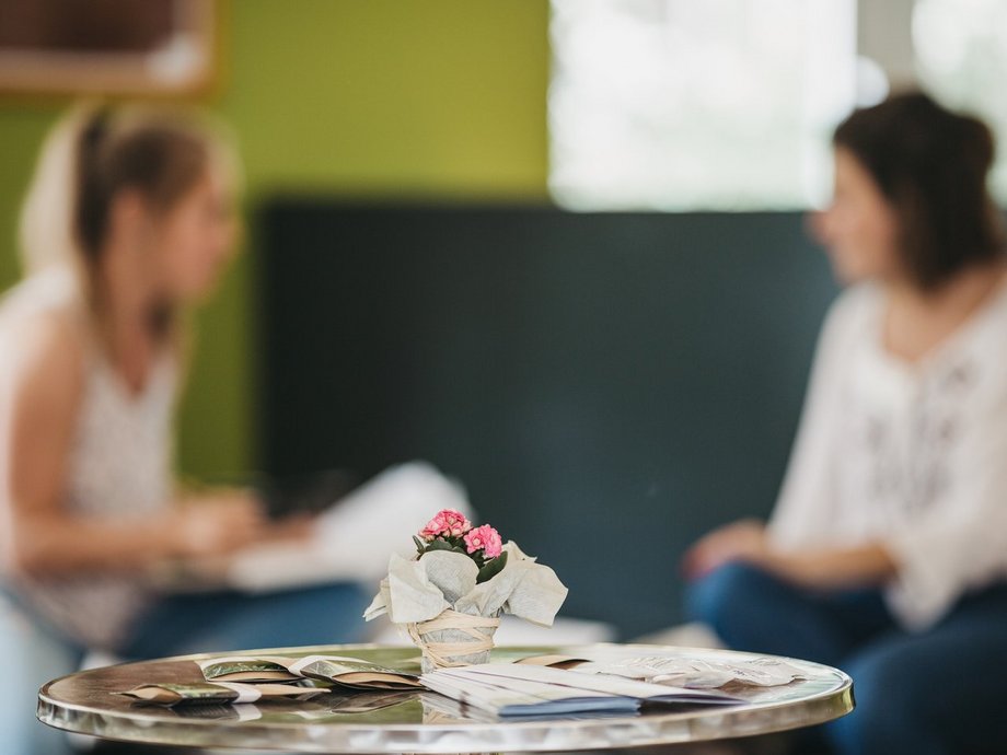 Ein Tisch mit Blumendekokaration, im Hintergrund sind zwei Studentinnen im Gespräch.