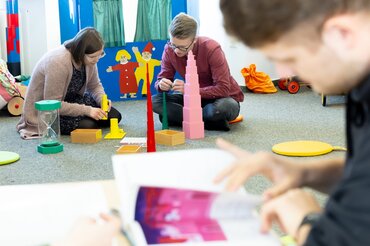 Zwei Studierende sitzen in einem Spielzimmer und bauen Türme.