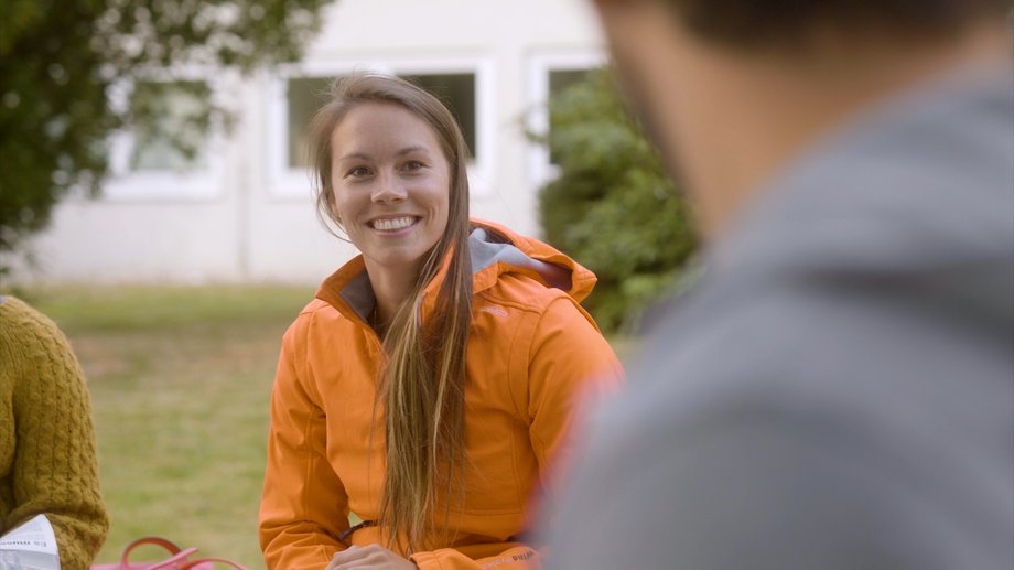 Eine junge Studierende lacht eine Person während eines Gesprächs an. Sie sitzen draußen auf dem Gelände der katho in Aachen.