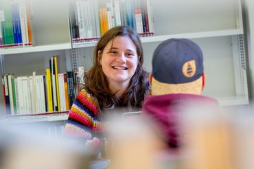 Zwei Studierende sitzen sich in der Bibliothek gegenüber und schauen sich an.