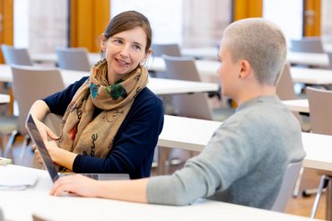 Studierende sitzen mit einer Dozentin an einem Tisch und reden miteinander.