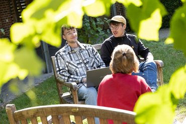 Mehrere Studierende sitzen zusammen im Außengelände und reden miteinander.