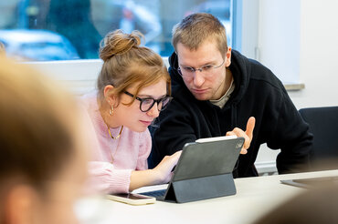 Zwei Studierende blicken konzentriert auf einem Bildschirm.

