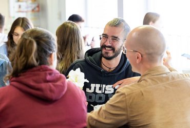 Mehrere Studierende sitzen in der Cafeteria an einem Tisch zusammen und reden.