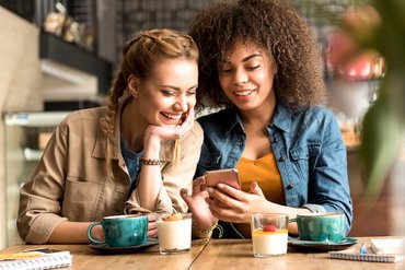 Zwei junge Frauen sitzen im Café schauen auf ein Handy.
