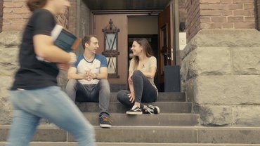 Ein junger Mann und eine junge Frau sitzen auf den Stufen des Paderborner katho-Hochschulgebäudes und unterhalten sich.
