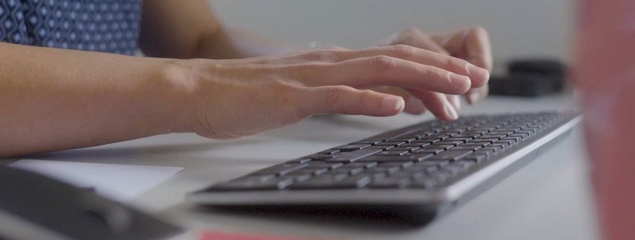Nahaufnahme der Hände einer Person, die etwas auf einer PC-Tastatur schreibt.