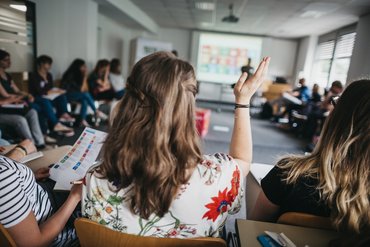Studierende im Sitzkreis, eine Studentin meldet sich.