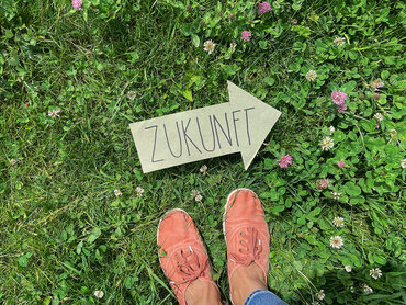 Person steht auf einer Wiese vor einem grünem Pfeil auf dem das Wort Zukunft geschrieben steht