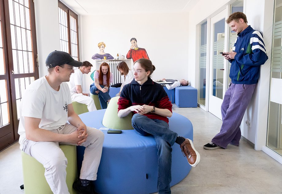 Mehrere Studierende halten sich in einem Aufenthaltsraum auf  und unterhalten sich, nutzen ihre Handys oder legen sich hin.