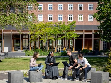 Mehrere Studierende halten sich im Außengelände auf und und unterhalten sich.
